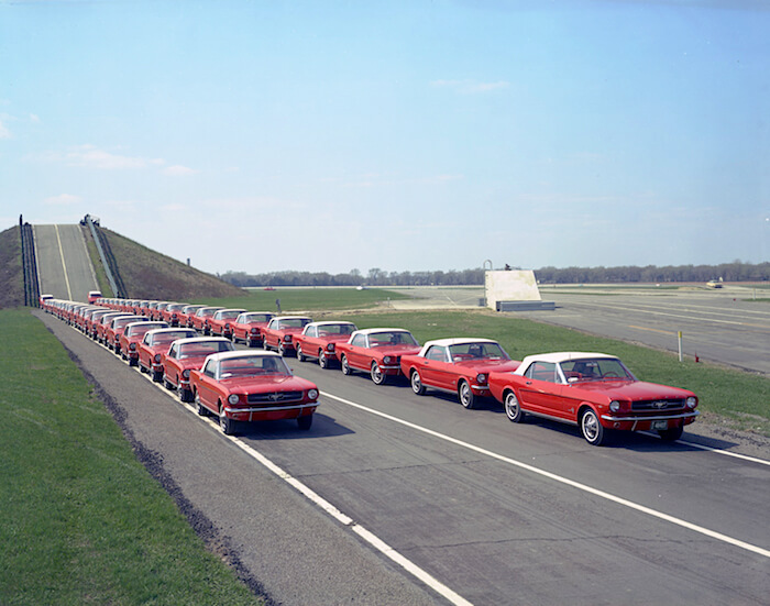 Vuosimallin 1964 punaisia Ford Mustangeja jonossa tekstiradalla. Kuvan copyright: Ford Motor Company.